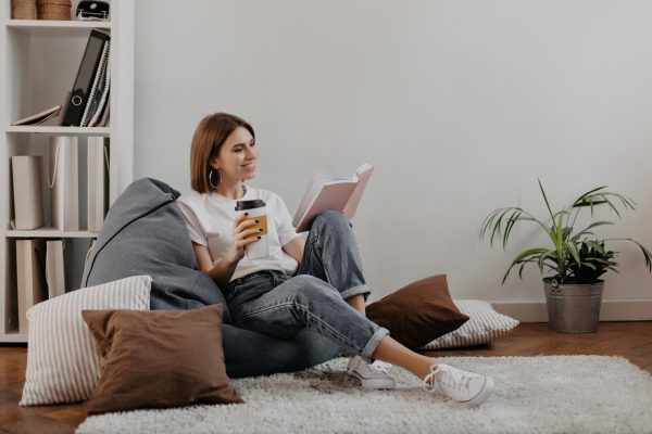 short-haired-girl-white-t-shirt-with-smile-reading-book-while-sitting-soft-bean-bag